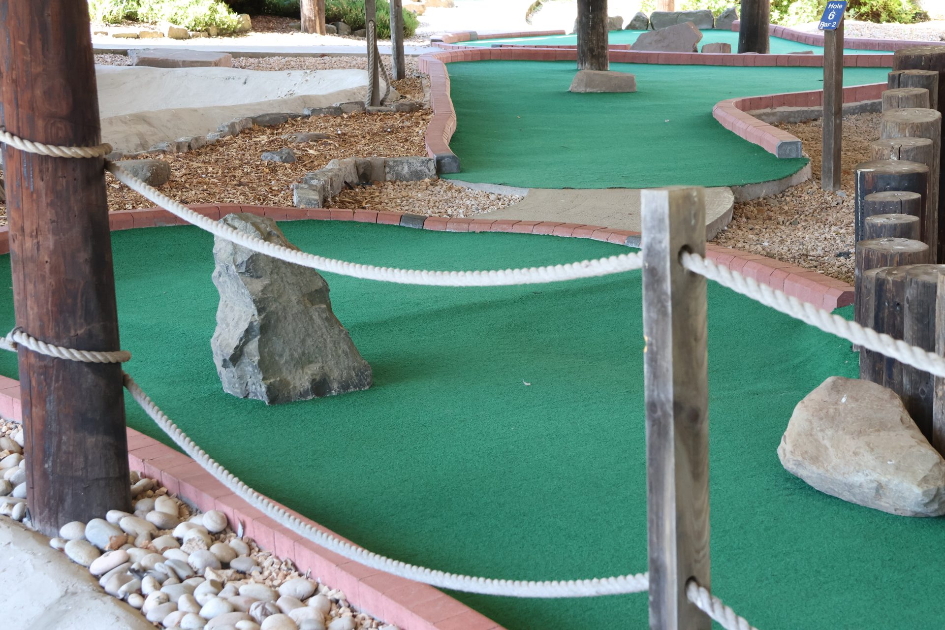 Covered adventure golf hole with rocks and rope fencing